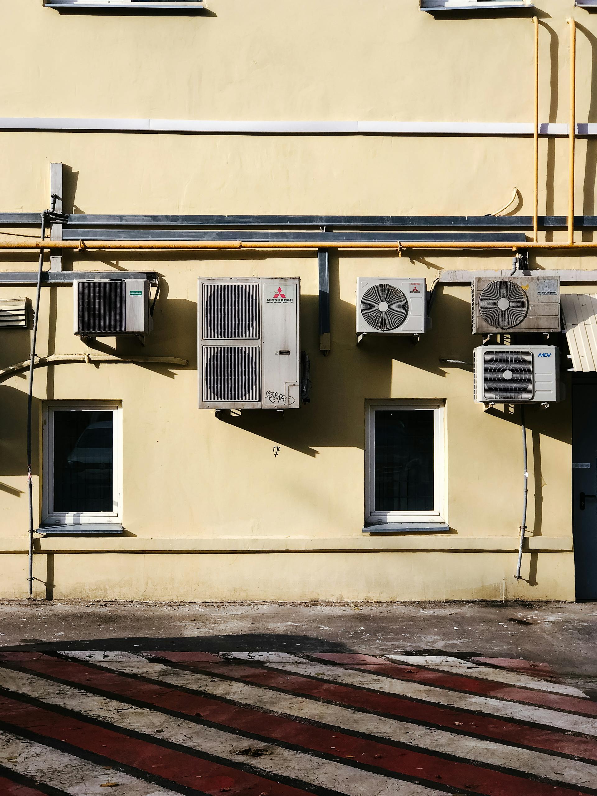 Yellow building facade with multiple air conditioning units mounted on wall.